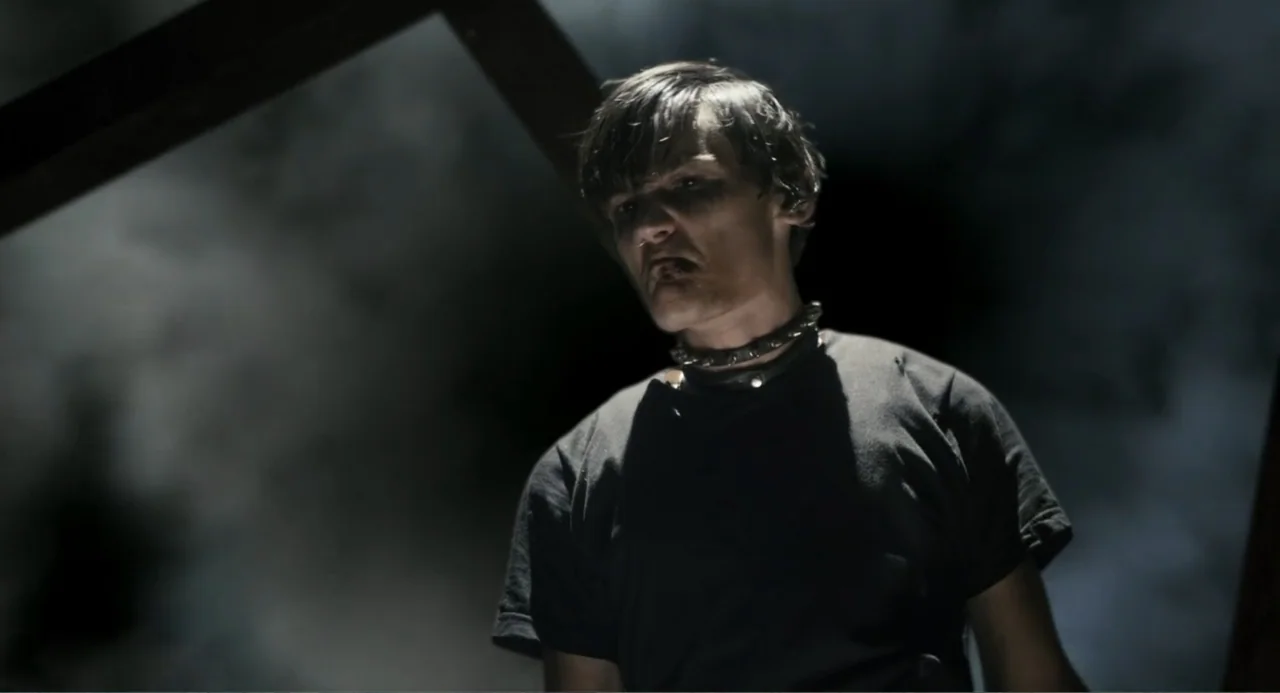 Gates of Darkness (2019) movie still: medium — A dark, smoky environment surrounds a young man against an indistinct background. The man looks…