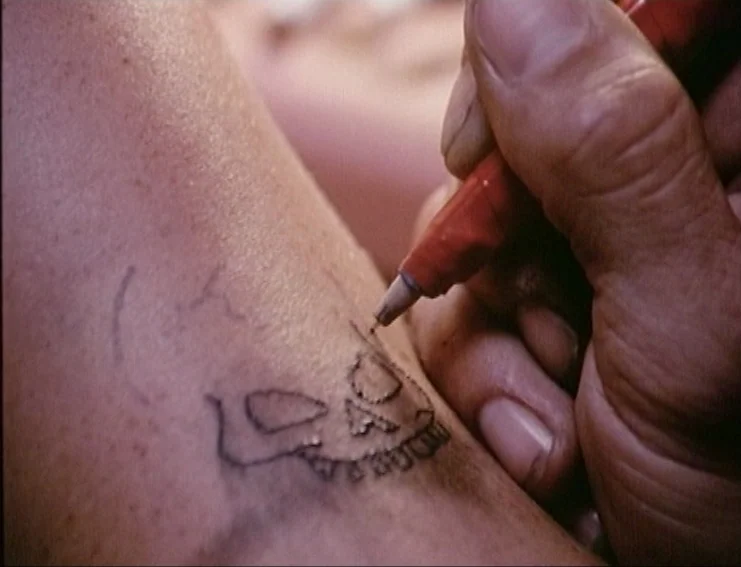 Ghosts… Of The Civil Dead (1988) movie still: closeup — A close-up view of skin marked with a hand-drawn ink outline of a skull. A hand holds a red…