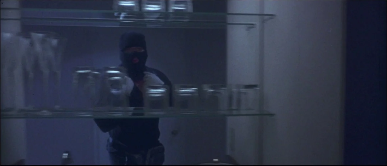 Strange Days (1995) movie still: medium — A dimly lit room features a stacked glass shelf display containing multiple drinking glasses. A figure…