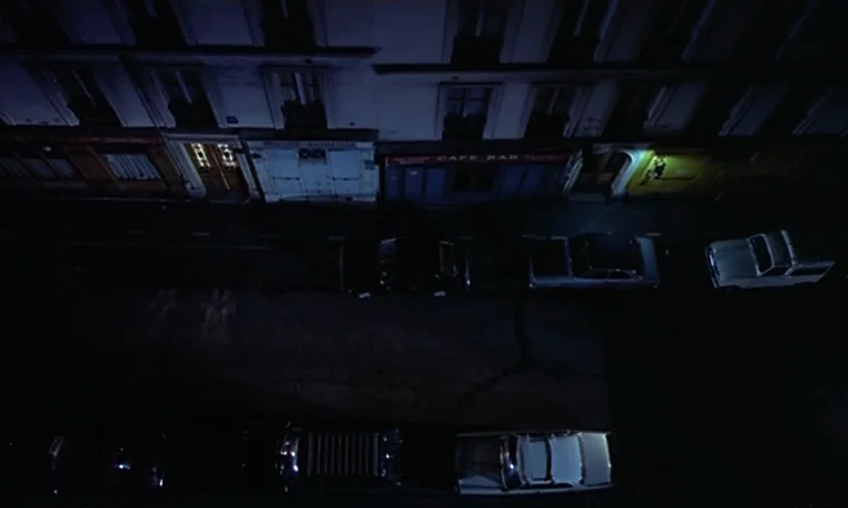 Nuits Rouges (1974) movie still: wide — A quiet urban street at night lined with parked cars and multi-story apartment buildings. The scene shows…
