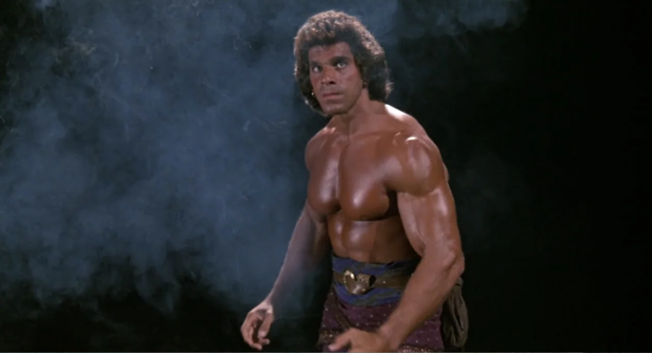 Hercules (1983) movie still: medium — A man with a highly muscular physique stands amidst thick swirling smoke against blackness. He wears a…