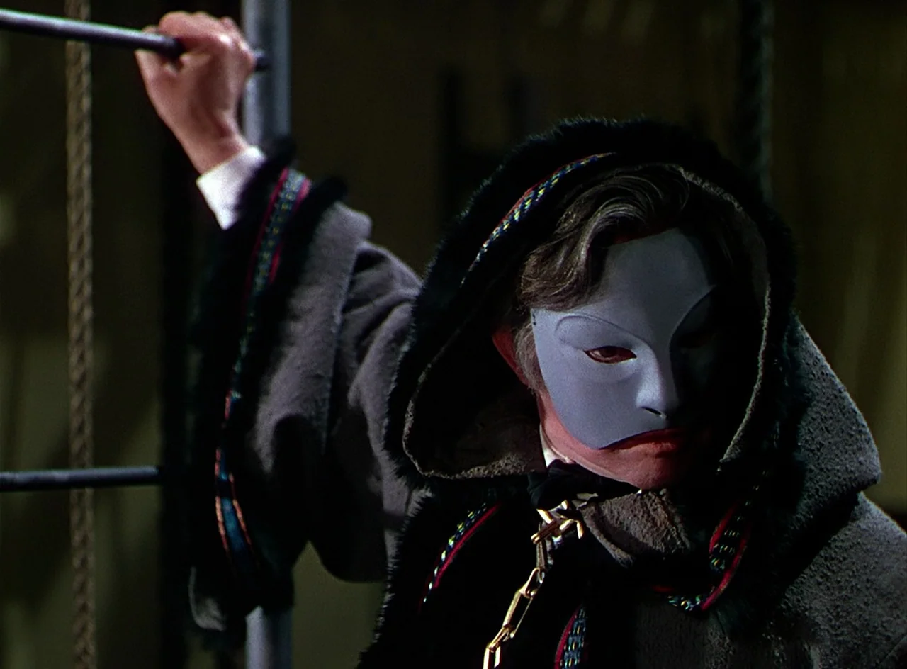 Phantom of the Opera (1943) movie still: medium — A dark indoor space featuring a person wearing a formal gray eye mask. The subject grasps a…