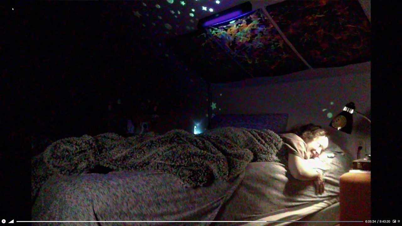 We’re All Going to the World’s Fair (2021) movie still: medium — A dark bedroom features a bed illuminated by a small bedside lamp. A person lies…