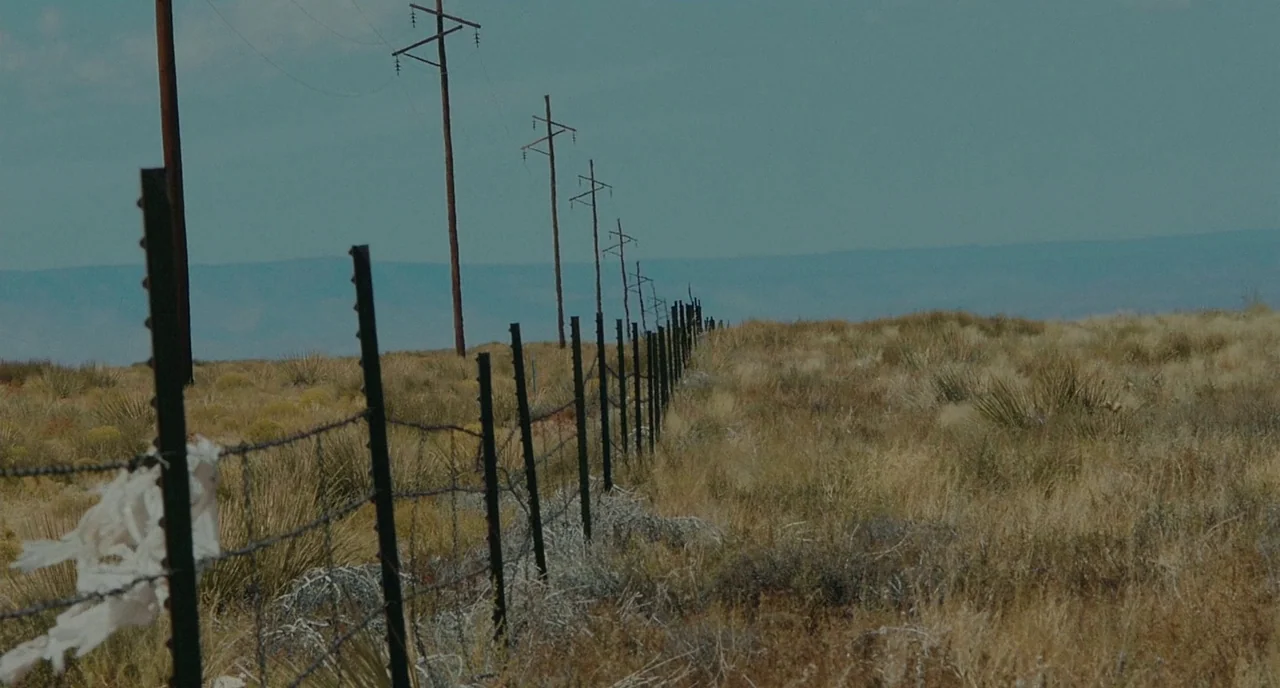 Fast Color (2018) movie still: wide — A dry, grassy plain stretches toward a distant blue horizon under a hazy sky. A long black metal fence with…
