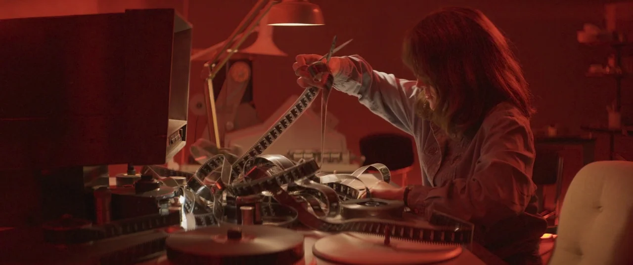 Daaaaaalí! (2023) movie still: medium — An editing suite illuminated by intense red light contains a film splicer and monitor. A woman sits at the…