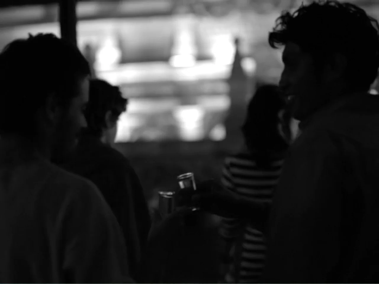 Güeros (2014) movie still: medium — A dimly lit bar interior contains two men clinking small glasses together in toast. The background features…