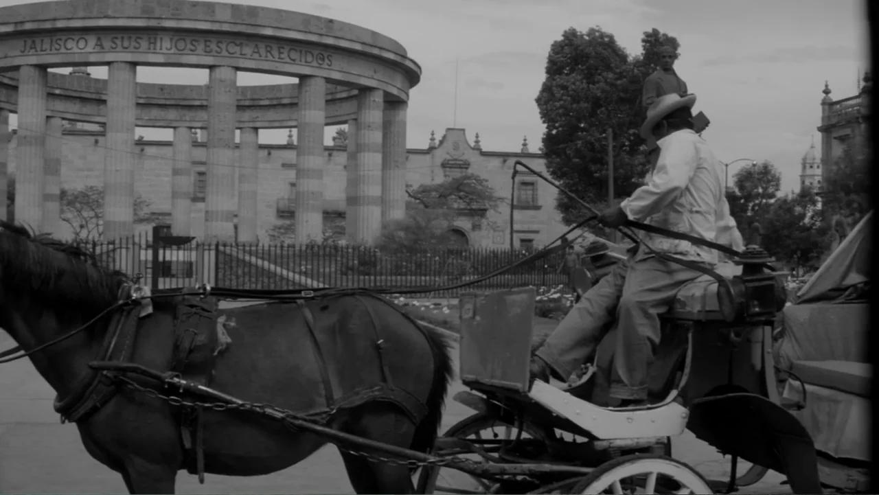 Escuela para solteras (1965) movie still: medium — A public plaza features a stone rotunda with large pillars and arched entrances. A man operates a…