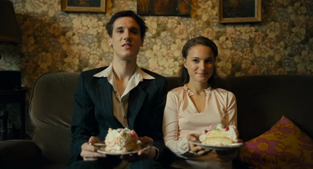 Paris, Je T’Aime (2006) movie still: medium — A living room features floral patterned wallpaper and framed pictures on the wall. A young man and…