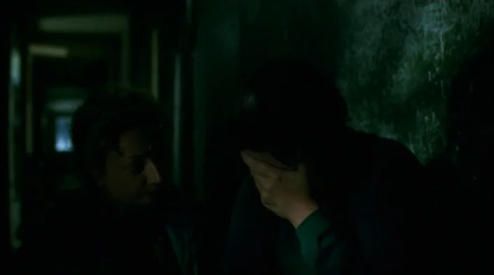 Code Unknown (2000) movie still: medium — A dimly lit, narrow corridor with dark, textured walls providing little visibility. Two women sit near…