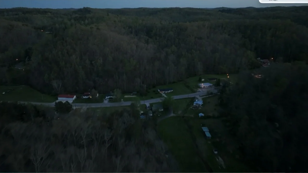 Murder at Carter County Mines (2023) movie still: establishing — An aerial view of a rural valley with forested hills and small residential houses.…