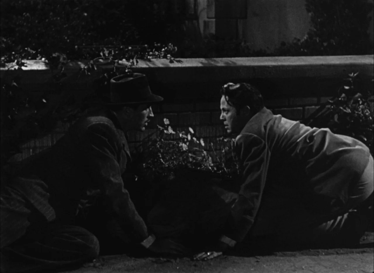 House by the River (1950) movie still: fullbody — Two men crouch on a paved surface against a low brick wall at night. They face one another while…