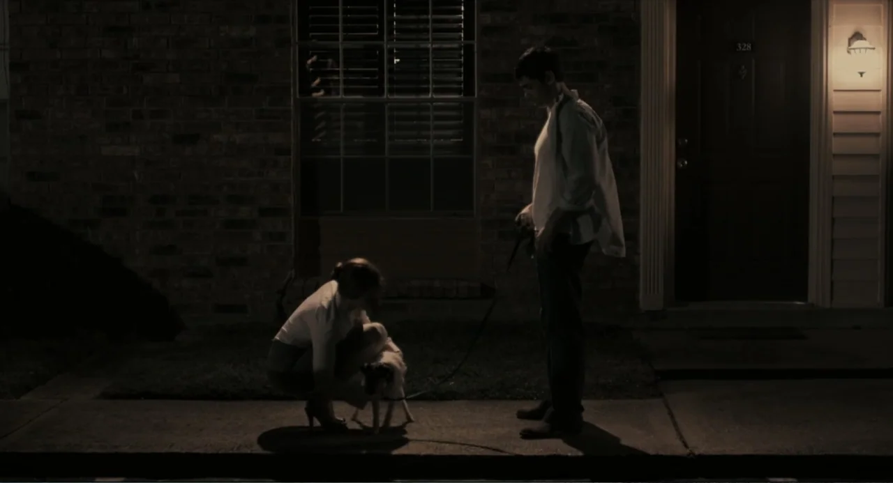 Beyond a Reasonable Doubt (2009) movie still: fullbody — A dark residential sidewalk exterior at night features a brick building facade. A man…