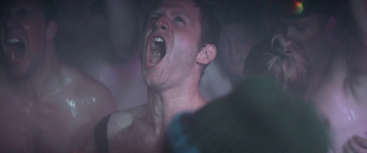 Force Majeure (2014) movie still: medium — A dark, crowded nightclub interior is filled with people in dim neon lighting. A man stands in the…