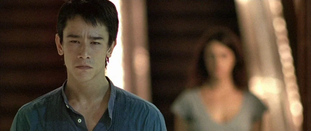 Boarding Gate (2007) movie still: medium — A narrow interior hallway with dark wood-paneled walls and soft natural lighting. A young man stands in…