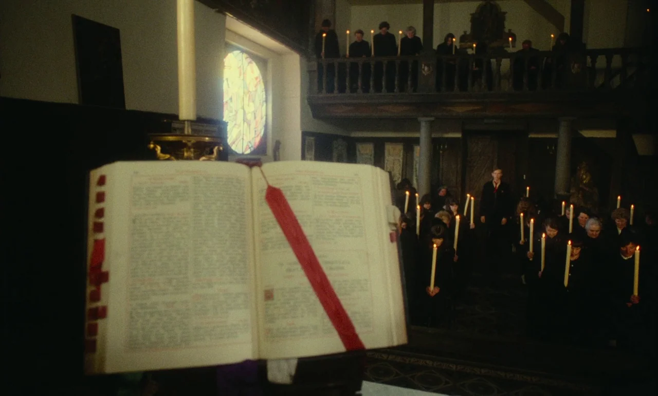 Litan (1982) movie still: wide — A church interior features a large open book on a lectern in the foreground. Numerous individuals stand in the pews…