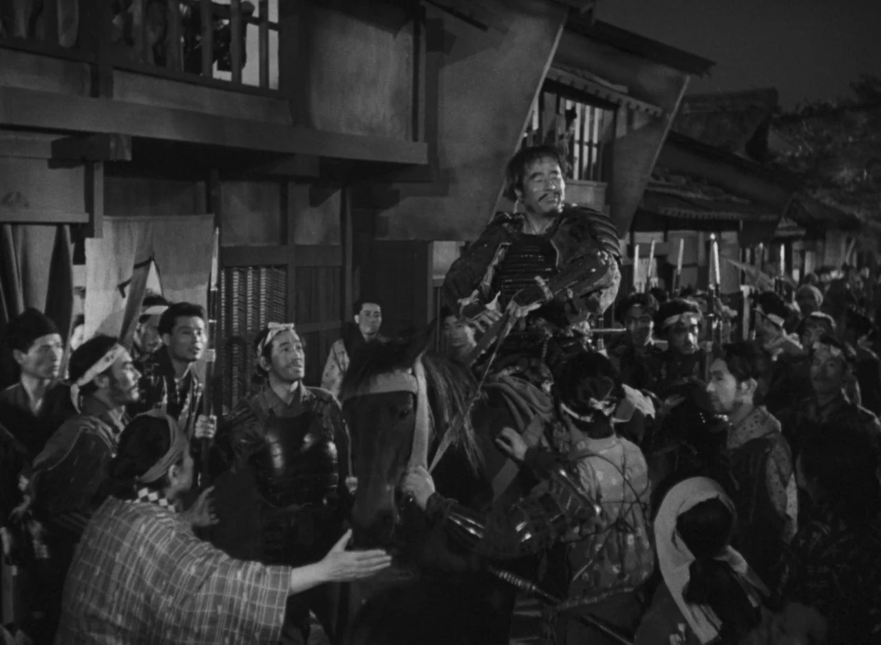 Ugetsu (1953) movie still: medium — A dense crowd of people surrounds a samurai on horseback in a night street. The wooden architecture of the…