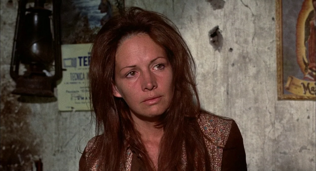 Bring Me The Head of Alfredo Garcia (1974) movie still: closeup — An interior space features aged, cracked plaster walls adorned with a religious…