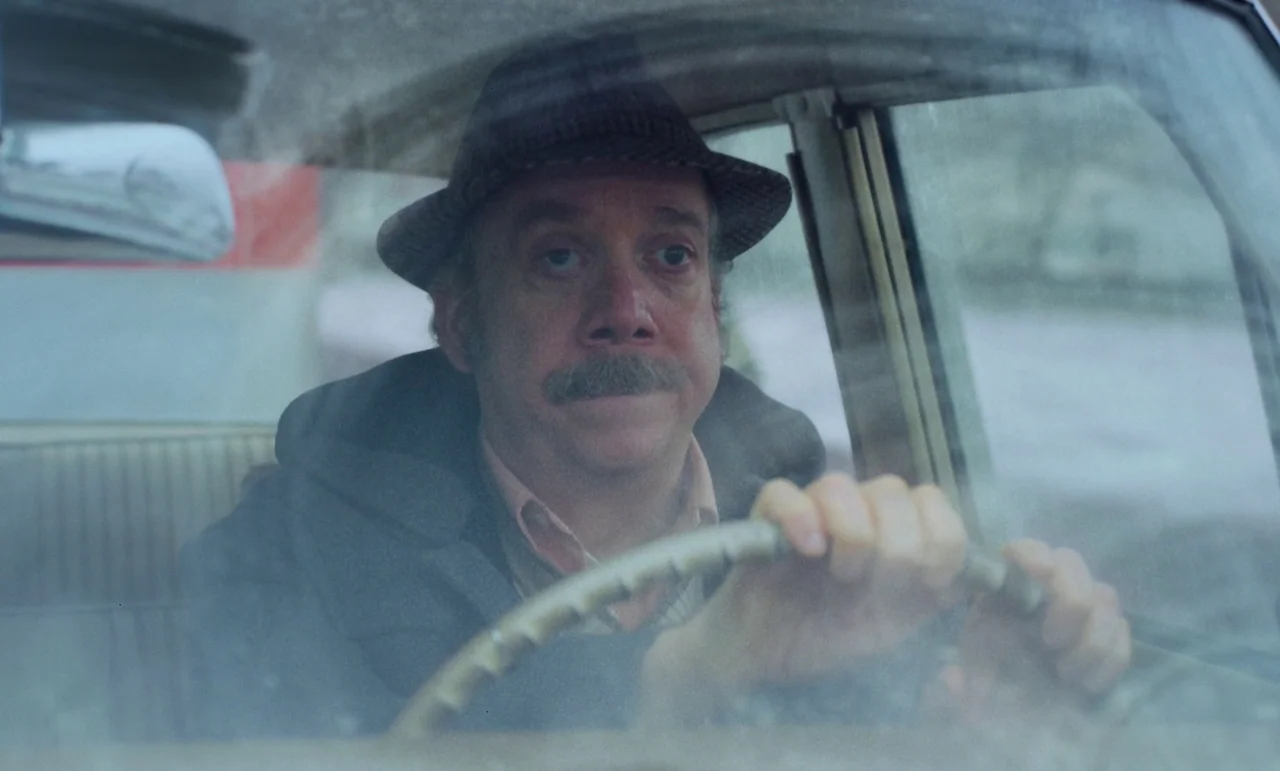 The Holdovers (2023) movie still: medium — A man drives a vintage car during the day. He sits behind the wheel and looks ahead through the windshield.