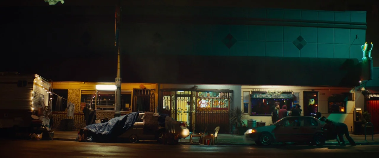 Sorry to Bother You (2018) movie still: wide — A night view of a low-rise commercial building with a faded teal facade. Several cars parked on the…