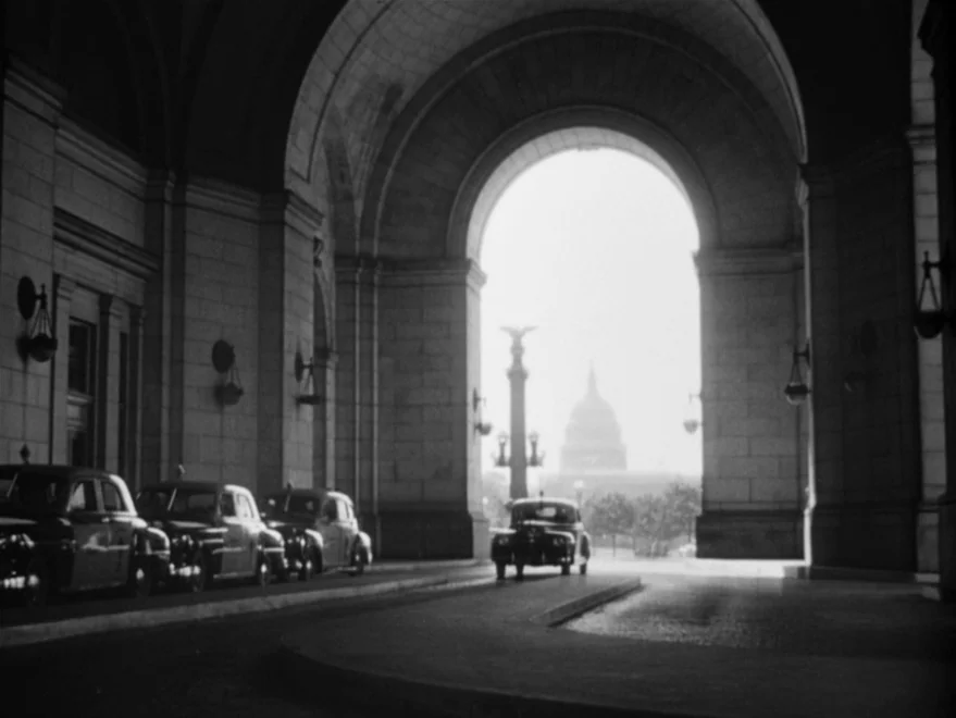Strangers on a Train (1951) movie still: wide — A stone masonry archway frames a view of the US Capitol building in distance. Several parked vintage…