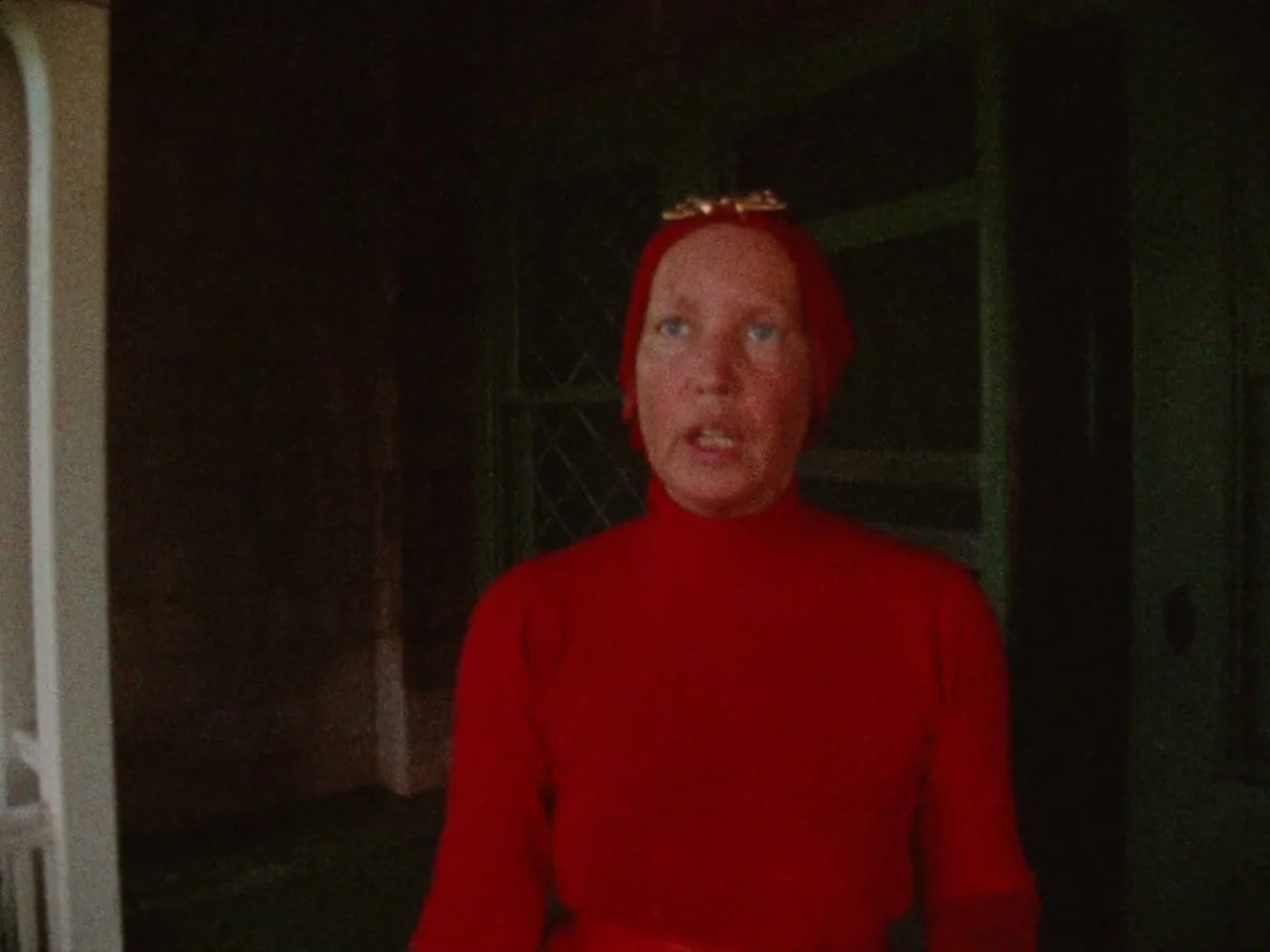 Grey Gardens (1975) movie still: medium — A dark, dimly lit indoor corridor features shadowed walls and minimal architectural detail. A woman wears…
