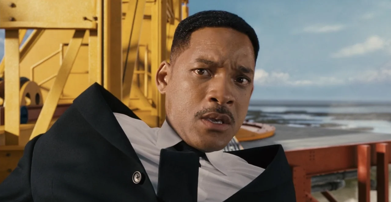 Men in Black 3 (2012) movie still: medium — An industrial metal structure towers in the background under a clear sky. A man in a dark suit looks…