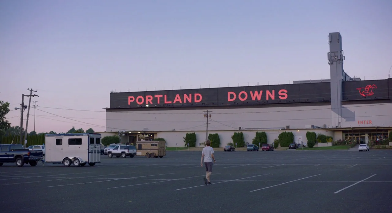 Lean on Pete (2017) movie still: wide — An expansive asphalt parking lot sits before a large, low-slung building with red neon signage. A single…