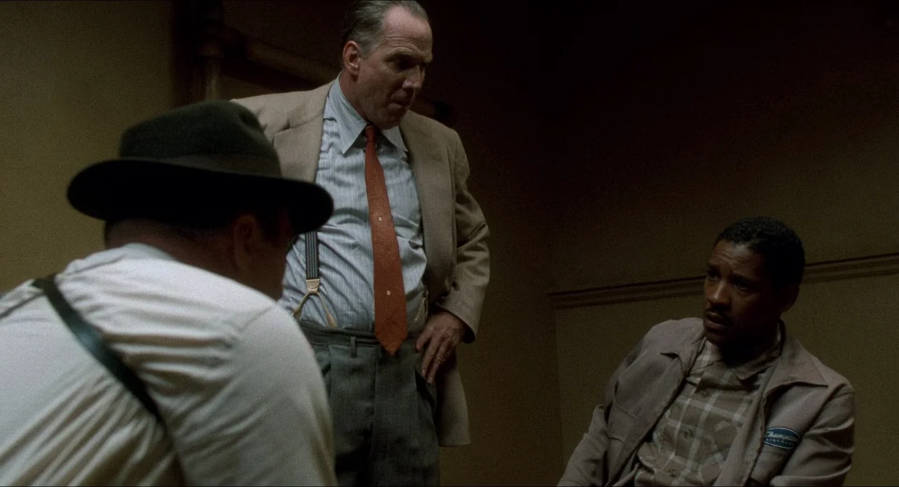Devil In A Blue Dress (1995) movie still: medium — A dimly lit room with plain walls and low overhead lighting suggests an interrogation. Three men…