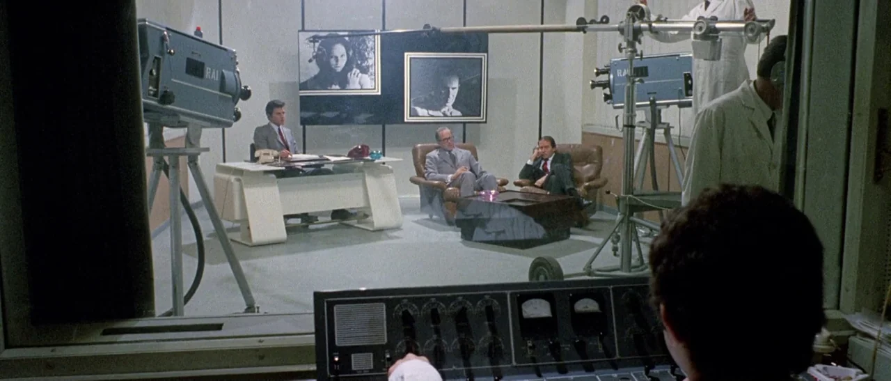 The Bird With The Crystal Plumage (1970) movie still: wide — A 1970s television studio set features white desks and leather armchairs. Three men sit…