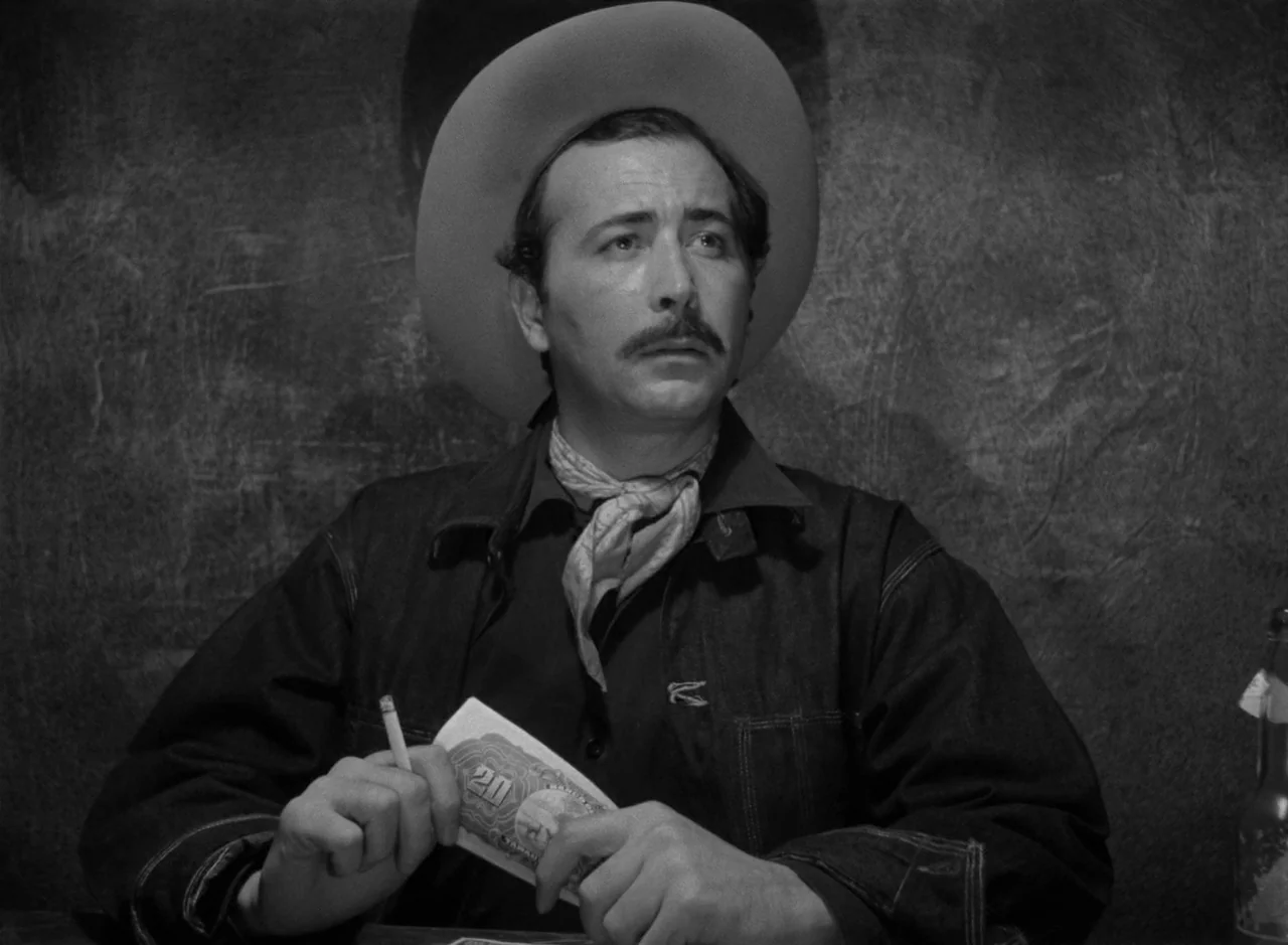 Victims of Sin (1951) movie still: medium — A dimly lit room features a subject against a rough-textured dark wall. The man sits at a table while…