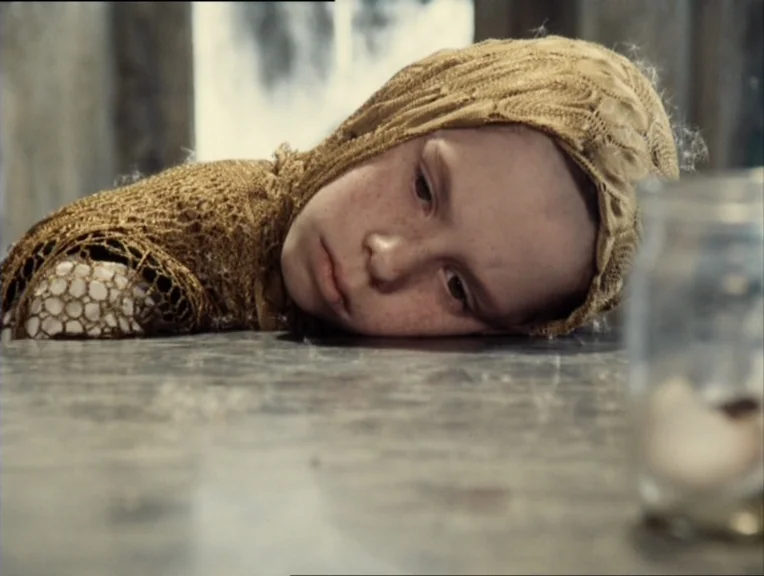 Stalker (1979) movie still: closeup — A light-colored wooden table surface serves as the setting for the child's repose. The subject leans their…
