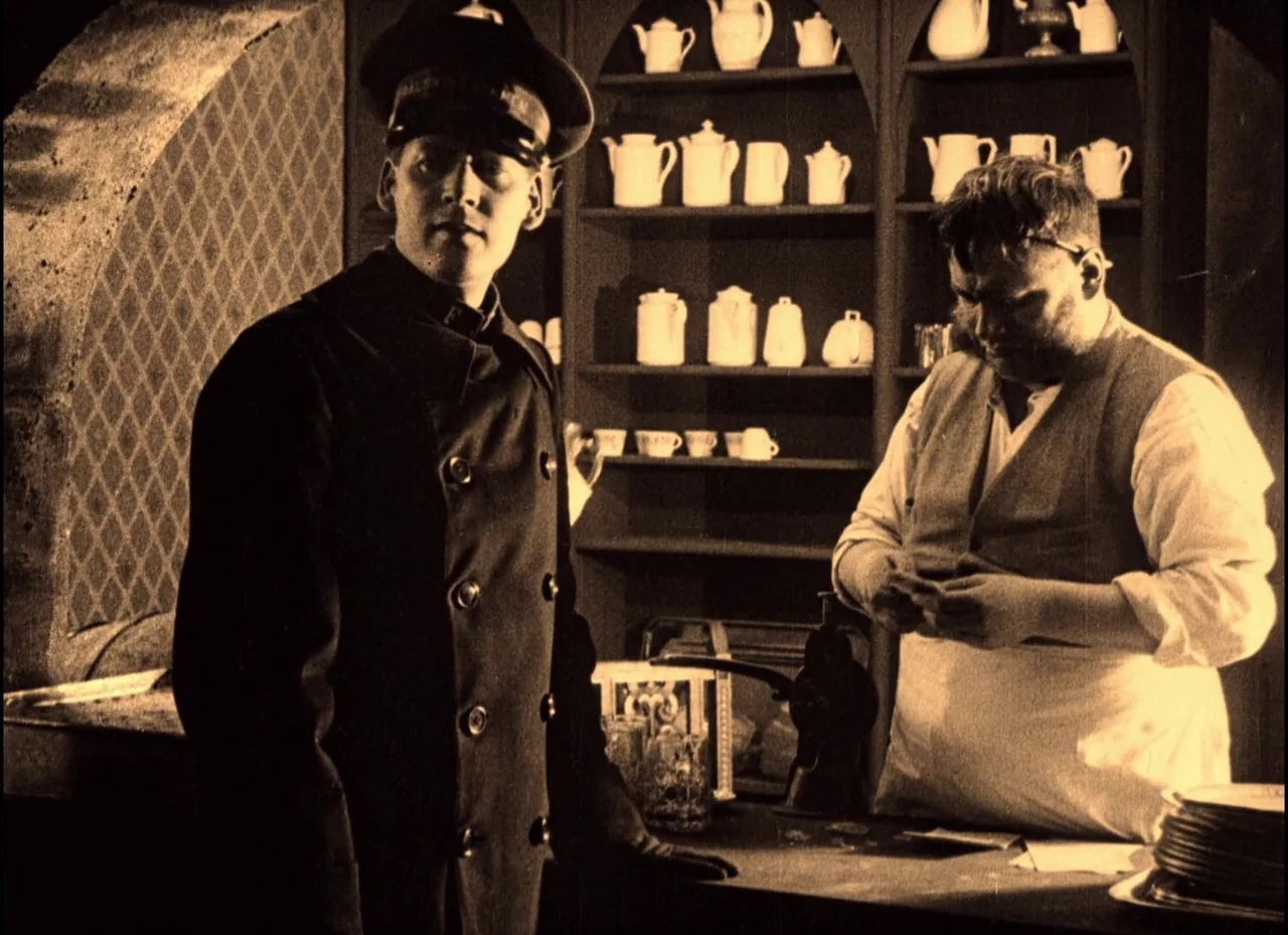 The Phantom Carriage (1921) movie still: medium — A dark store interior features shelves packed with rows of white ceramic pitchers and bowls. A…