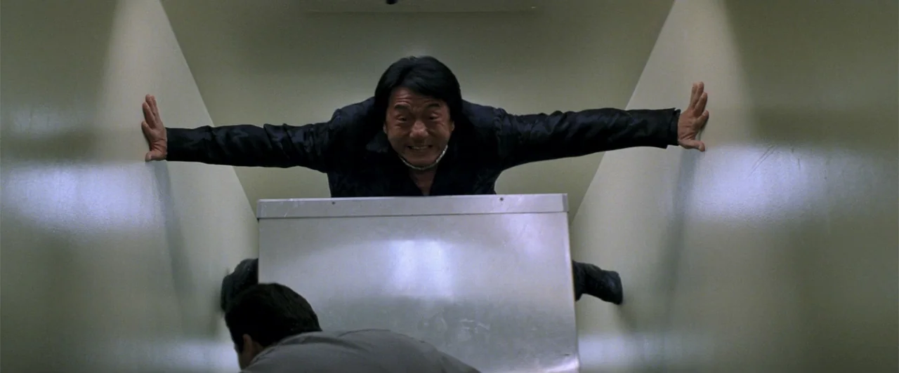 Rush Hour 2 (2001) movie still: medium — A narrow beige corridor with smooth, featureless walls. An athletic man holds himself horizontally between…
