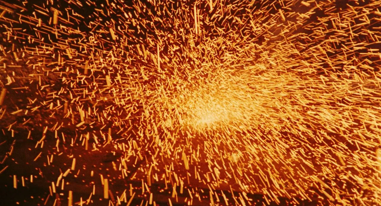 The Damned (1969) movie still: closeup — A dense cloud of glowing orange sparks radiates outward from a central hidden source. The background is…