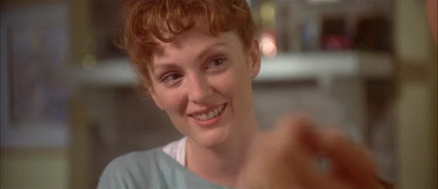 Short Cuts (1993) movie still: closeup — A domestic interior with a fireplace mantel visible in the blurred background. A woman with curly red hair…