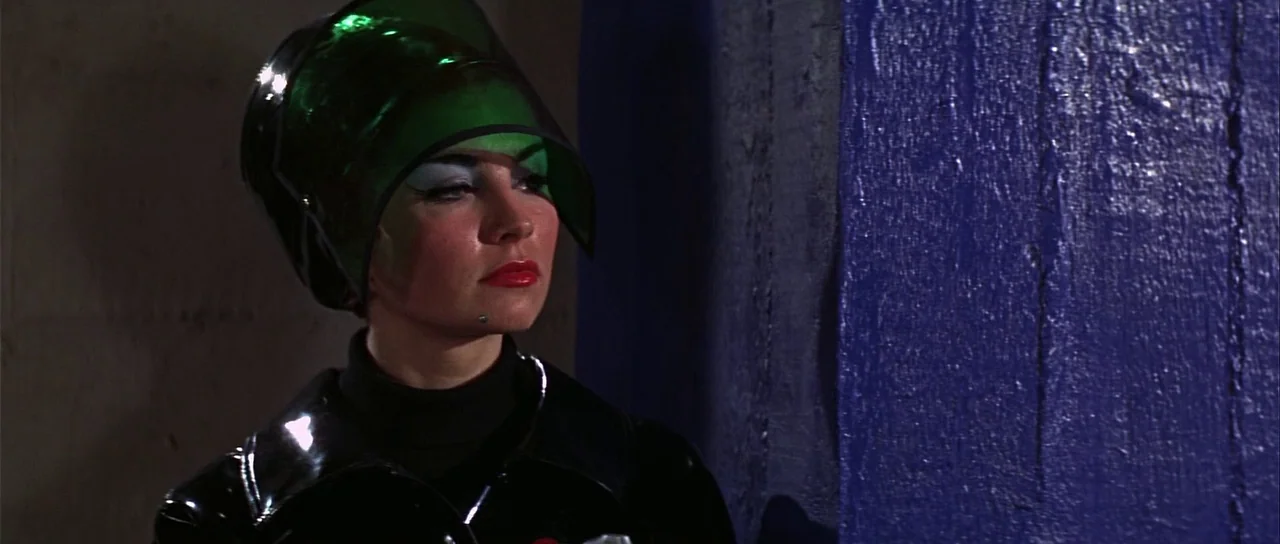 Casino Royale (1967) (1967) movie still: closeup — A dark space features a textured, deep blue wall beside a concrete surface. A woman wearing a…