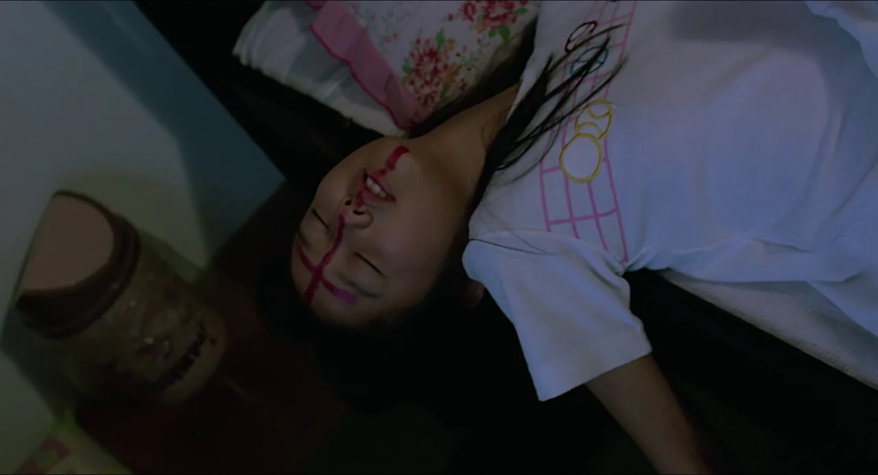 Typhoon Club (1985) movie still: closeup — A person lies on a mattress with a patterned pillow under their head. The subject remains motionless with…