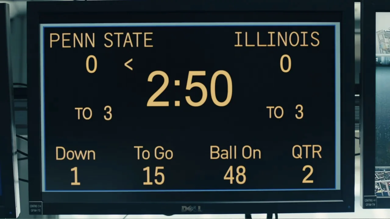 Paterno (2018) movie still: closeup — A close-up shot of a digital computer monitor displaying an American football scoreboard. The screen shows…