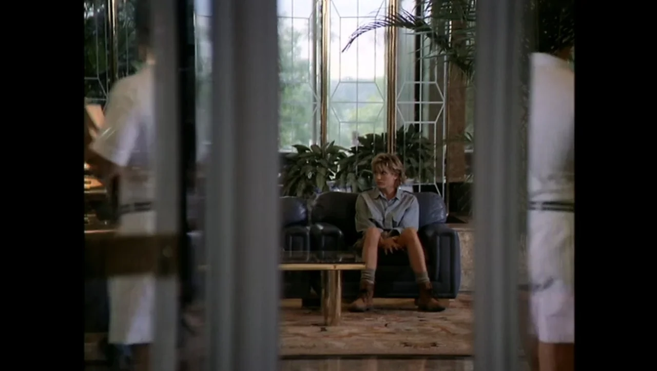 The Awakening (1995) movie still: medium — A spacious hotel lobby features large windows, potted plants, and dark leather furniture. A young woman…