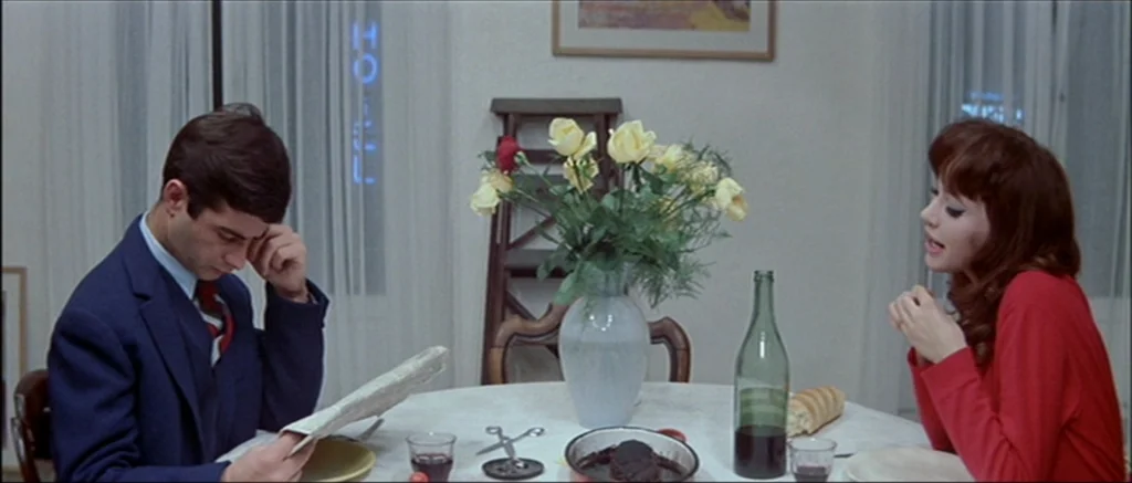 Une Femme Est Une Femme (A Woman Is a Woman) (1961) movie still: medium — A light-colored hotel room features a circular dining table set for a…