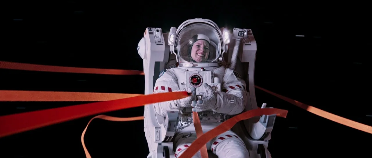 The Martian (2015) movie still: medium — A female astronaut in a bulky white space suit floats in deep, dark space. She grips multiple bright orange…