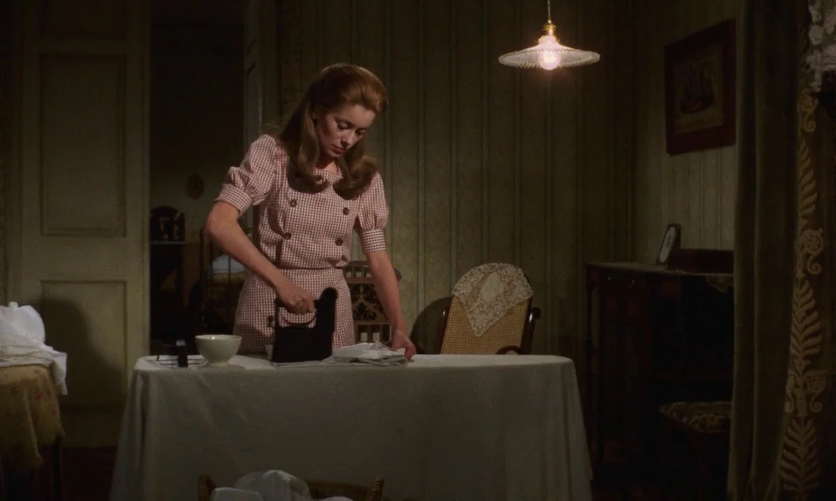 Tristana (1970) movie still: medium — A room features patterned wallpaper and a hanging pendant light above a table. A woman stands by the table…