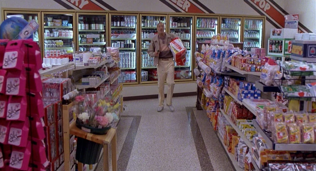 Raising Arizona (1987) movie still: fullbody — A well-stocked convenience store aisle with refrigerated beverage cases in the back. A man walks down…