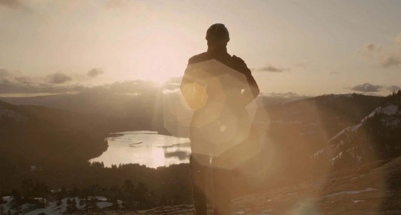 Her (2013) movie still: fullbody — A snowy mountain ridge overlooks a valley with a lake during golden hour. A man stands at the edge of the ridge…