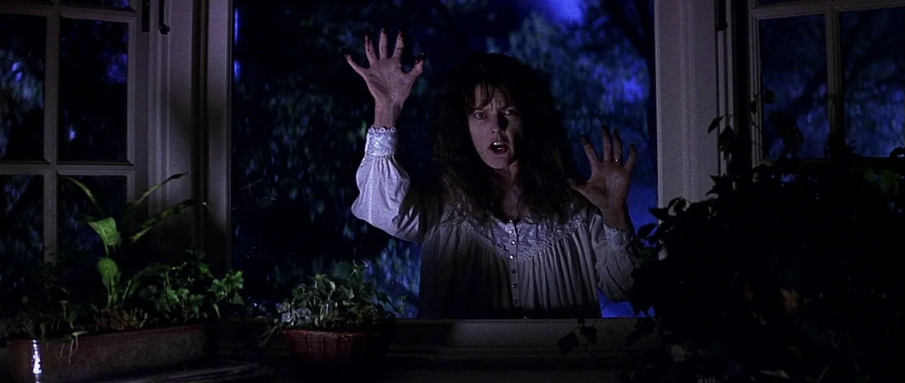 Scream 3 (2000) movie still: medium — A woman stands outside a paneled glass window at night under blue moonlight. She holds her hands against the…