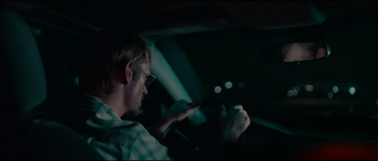 Sympathy For The Devil (2023) movie still: medium — The interior of a car at night with a blurred dark road visible through windows. A man with…