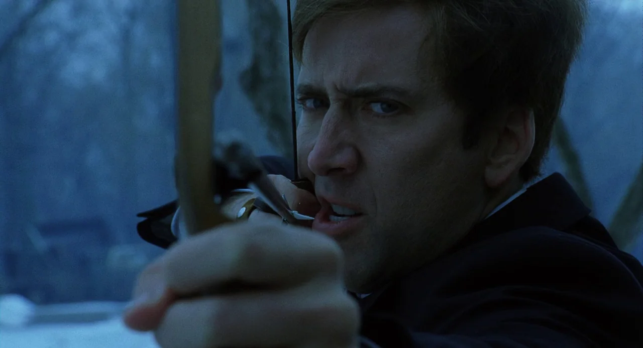 The Weather Man (2005) movie still: closeup — A man stands in a dark, wooded area during the blue hour. He aims an arrow forward while looking…