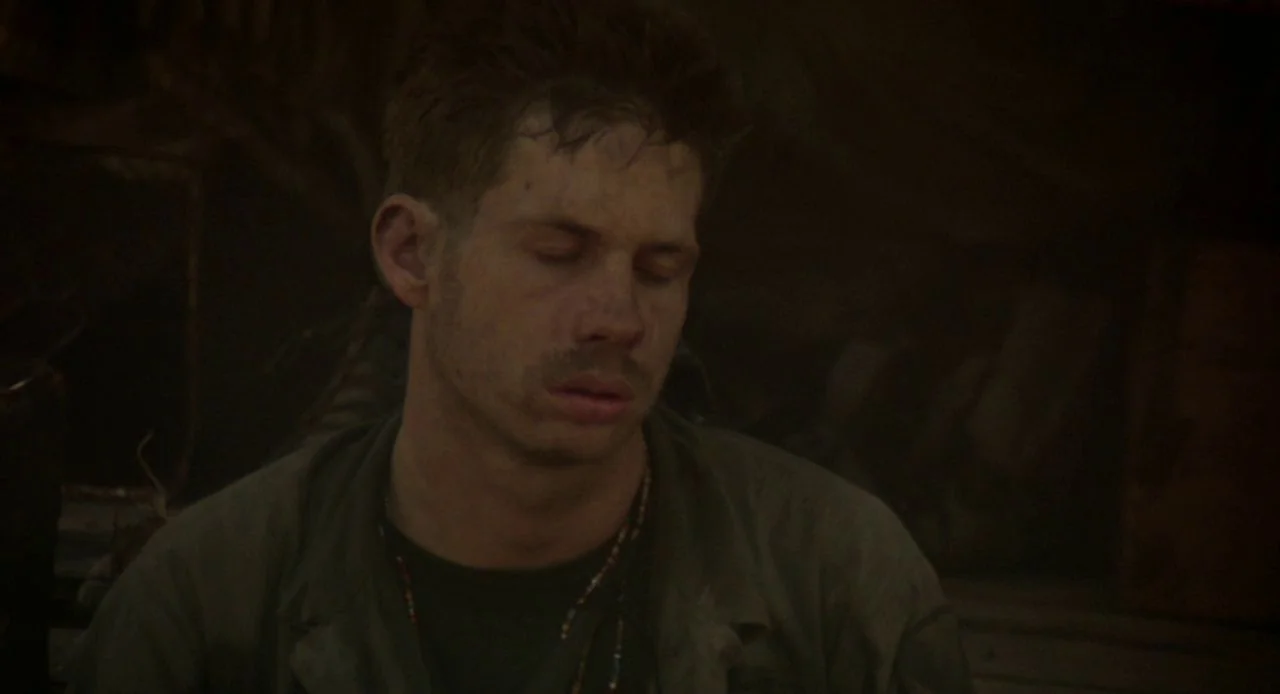Jacob’s Ladder (1990) movie still: medium — A dimly lit, enclosed space with dark walls and indistinct equipment in the background. A young man…