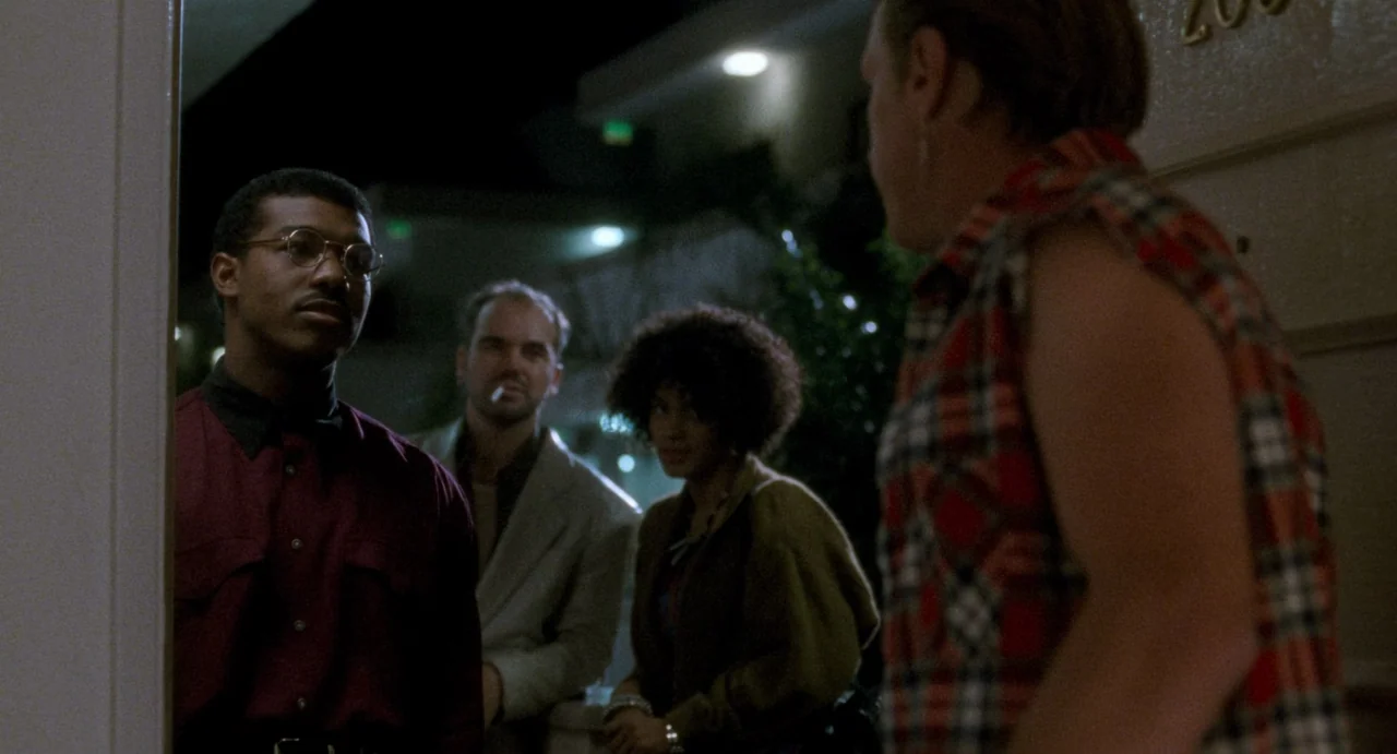 One False Move (1991) movie still: medium — A group stands outside a door at night near a lighted motel building. The figures occupy a walkway as…