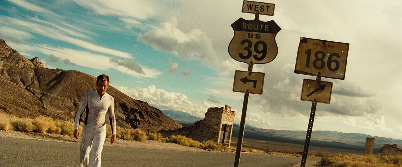 The Island (2005) movie still: wide — A desolate desert landscape features a cracked asphalt road and distant rocky mountains. A man in a white…